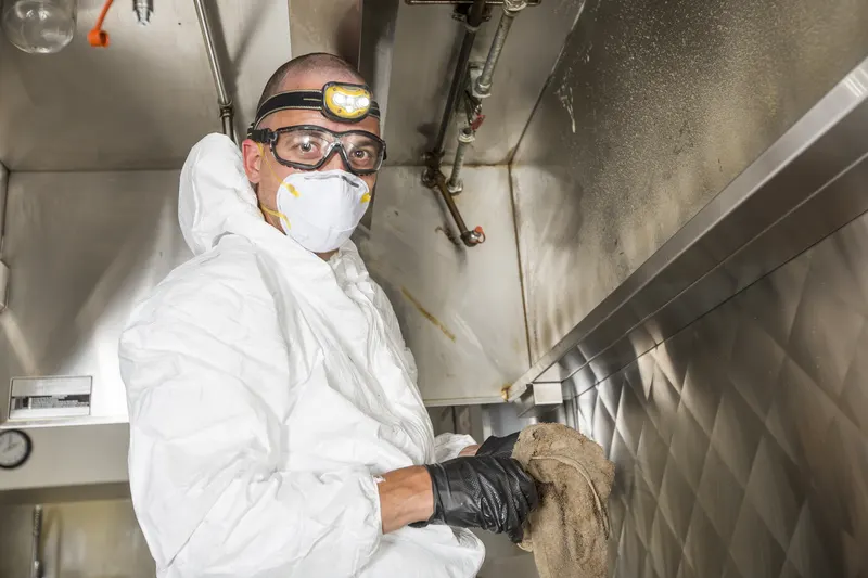 Technician in a headlamp, goggles and a mask wiping the lower lip of a stainless canopy