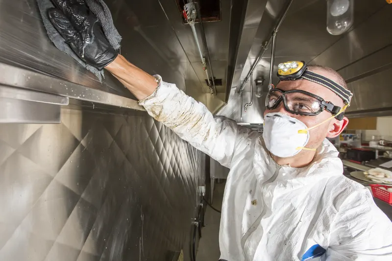 Technician reaching up to wipe the underside of a stainless canopy with a gloved hand