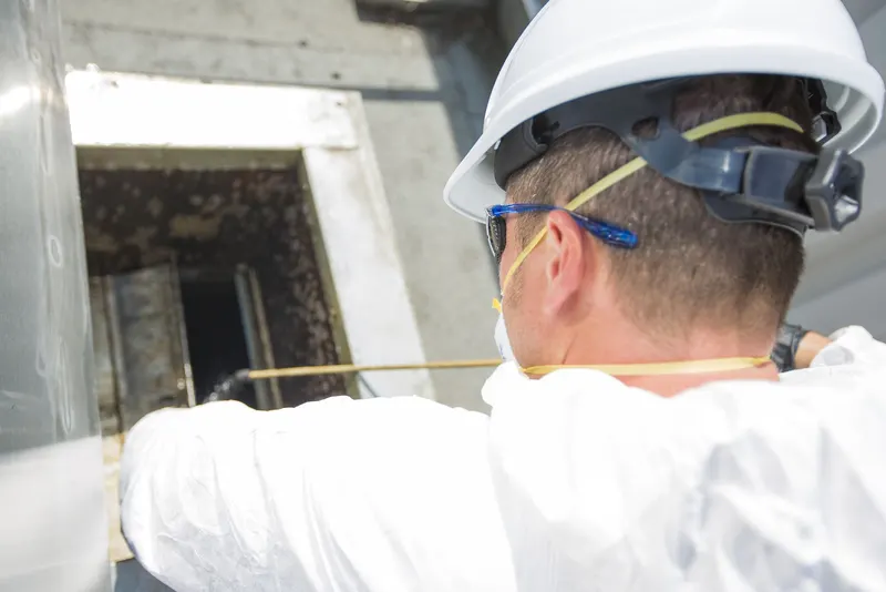 Technician in a hard hat looking down into an open rooftop exhaust duct