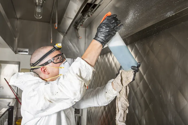 Technician spraying degreaser into the corner of a stainless exhaust hood