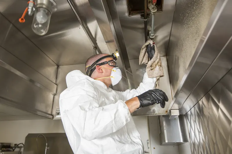 Technician wiping the filter track inside an exhaust hood with a cloth, a pendant light overhead